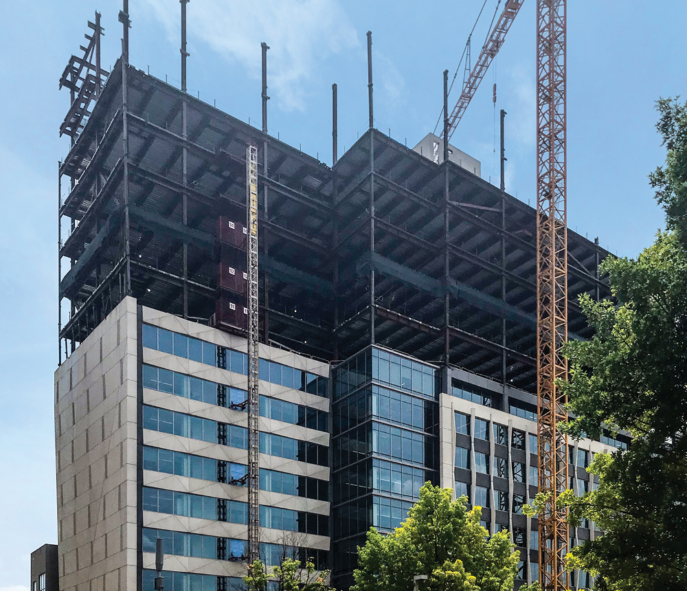 A building under construction is 10 stories tall with framing built on top for several additional stories and a crane still adding more.